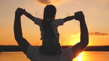 快乐的爸爸把一个小孩抱在肩上，在日落时分举起双手。父亲节。一个带着父母的孩子梦想着在黎明的背景下飞行。家庭生活
